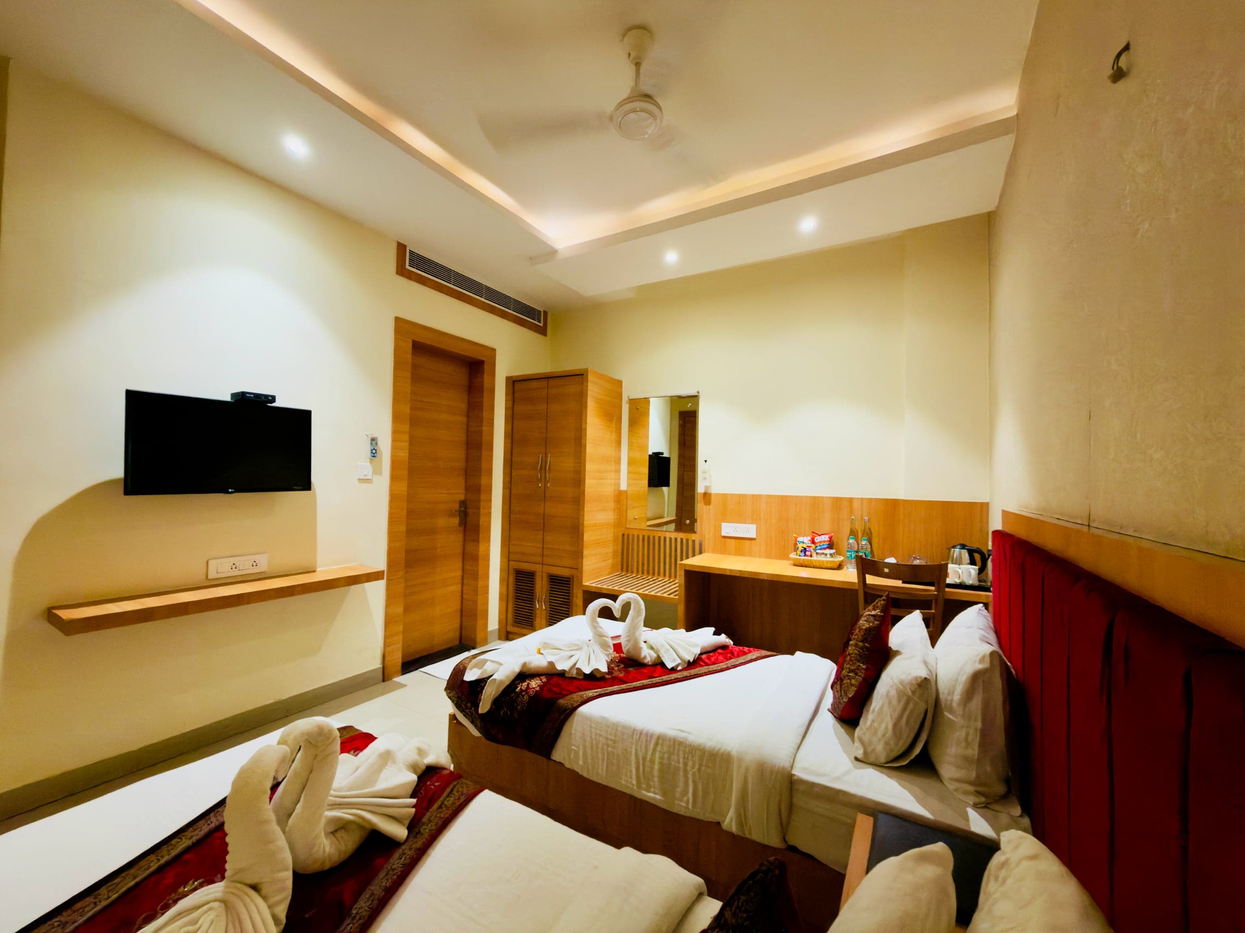 Deluxe room at Hotel Vagmi - king bed with deep-red velvet headboard, hand-folded towel swans, warm cove lighting