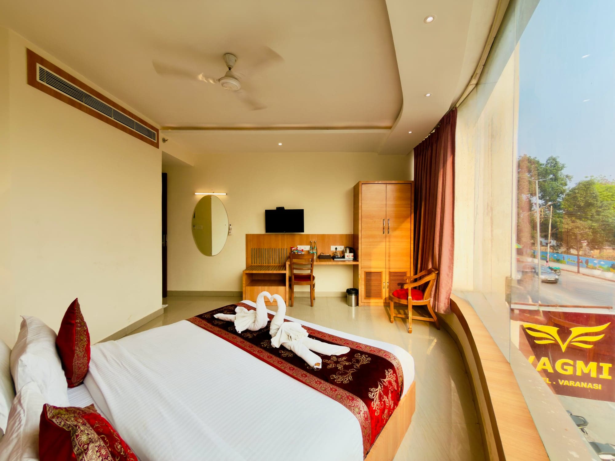 Executive room picture window with the Vagmi facade sign visible outside, bed dressed in red and white