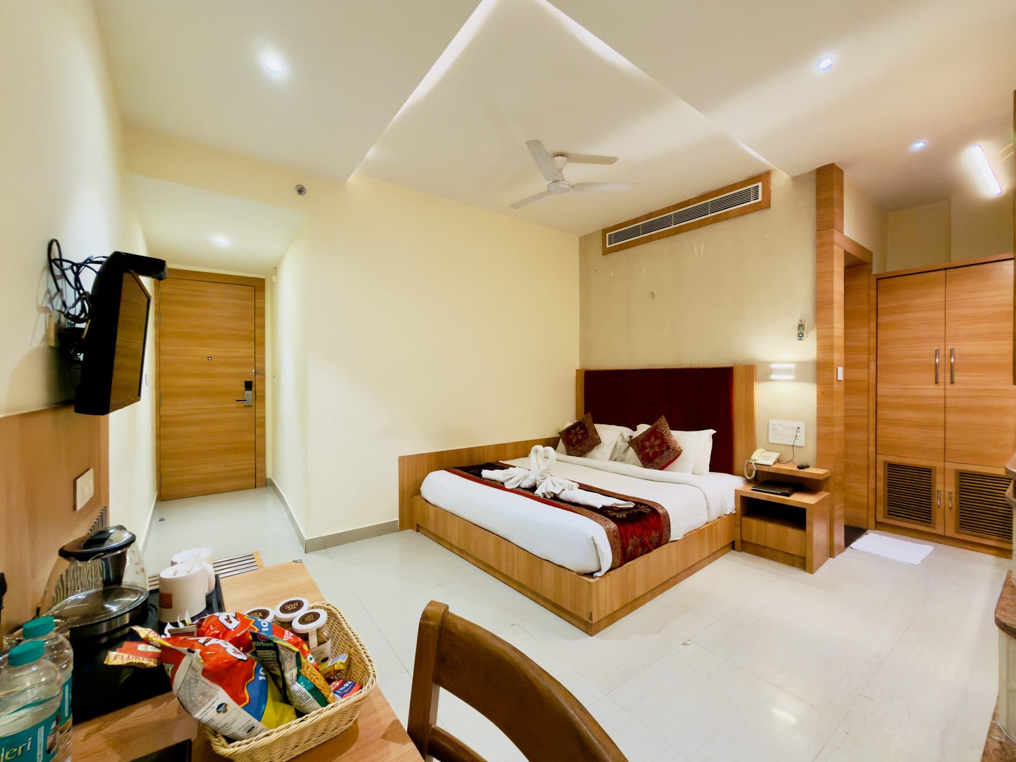 Executive room at Hotel Vagmi - king bed with deep-red velvet headboard, entry hall and wardrobe in warm wood